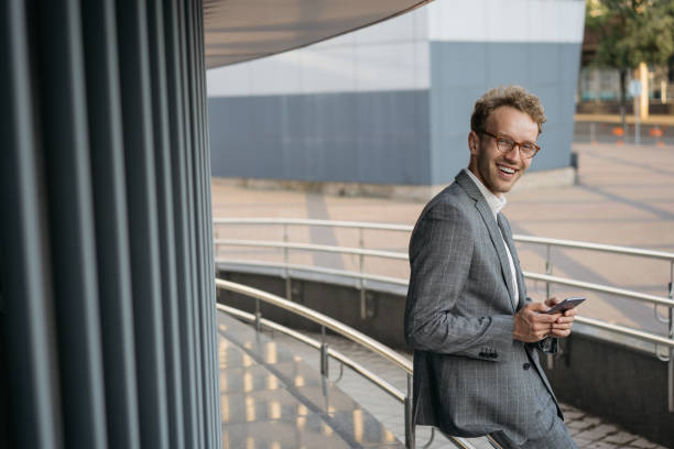 Handsome smiling businessman wearing suit, stylish eyeglasses using mobile phone, communication online, text messaging