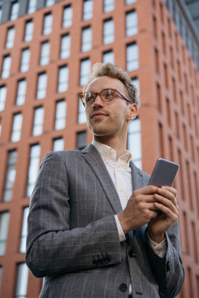istock Handsome businessman wearing stylish suit, hipster eyeglasses using mobile phone, communication online, looking away on the street 1344118883