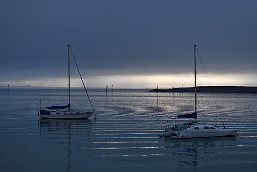 Sailboat moored in the harbour against the sunset. The seawater is cloudy.