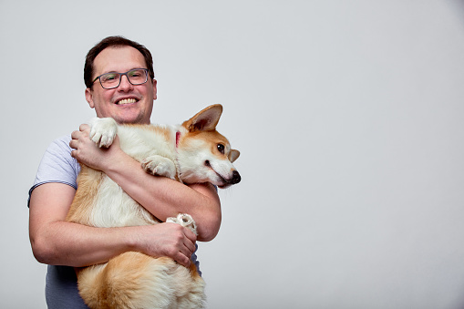 The dog lies on the shoulder of its owner. Welsh Corgi in his owner's hands on white background. The concept of people and animals. The guy holds his dog in his arms and plays with him. Copy space