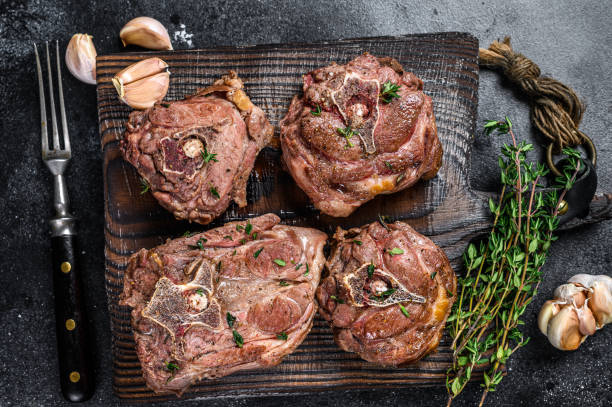 gegrillte lammhalsfleischsteaks auf einem holzbrett mit kräutern. schwarzer hintergrund. draufsicht - stewing steak stock-fotos und bilder