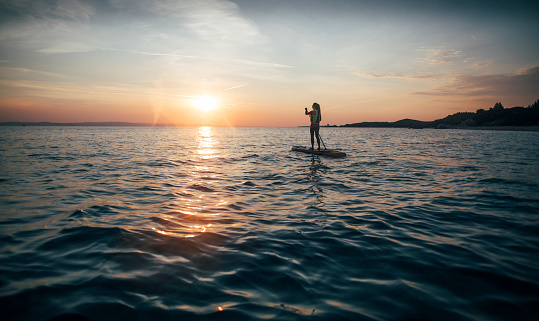 Woman on stand up paddle board enjoy sunset sea, copy space.