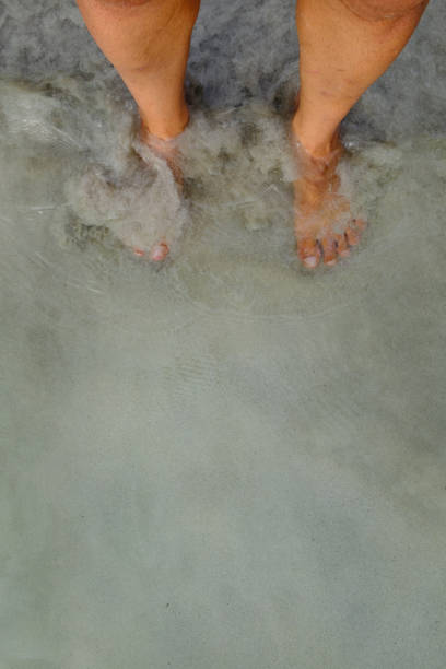Putting man feet inside the water wave on a sandy beach ground