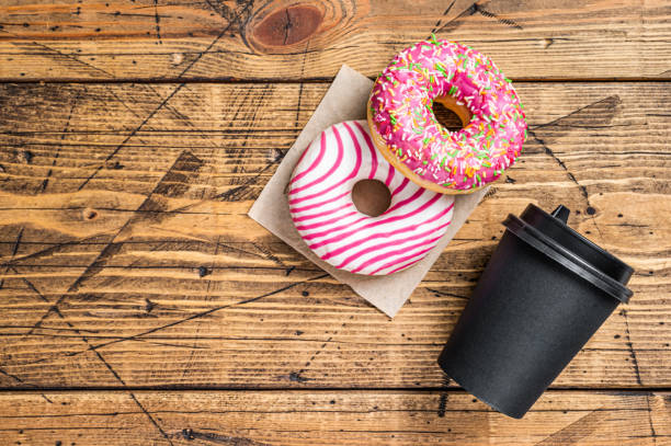 istock Pink glazed donuts on a kitchen table with coffee. Wooden background. Top view. Copy space 1344137890