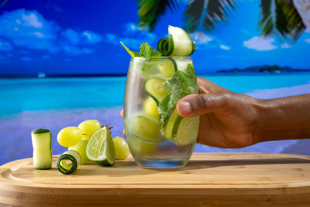istock refreshing cacktail glass decorated with grapes, cucumber and lemon, held by a male hand on a beach background 1344144678