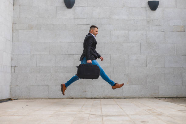 istock Handsome young white businessman rushing to work by taking huge steps while carrying a suitcase in an urban environment 1344144724