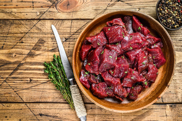 carne de venado silvestre cortada cruda para un goulash en un plato de madera. fondo de madera. vista superior. espacio de copia - carne de caza fotografías e imágenes de stock