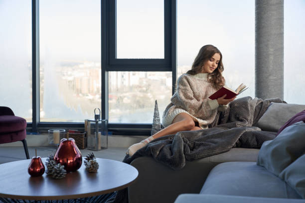 istock Pretty woman sitting on sofa and reading interesting book 1344156759
