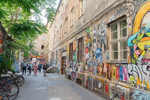 Berlin, Germany - August  27 2017; People walk along narrow lane bordered by old buildings with street art