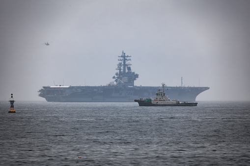 Yokosuka, Kanagawa Prefecture, Japan - May 19, 2021: The Japanese tug Uraga sits in Tokyo Bay as the USS Ronald Reagan deploys in the background from its homeport.
