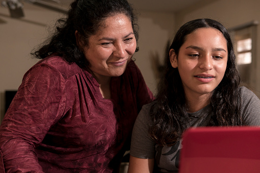 A teenager is showing something to her mom in a red laptop