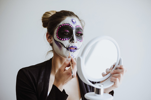 mexican Catrina, young latin woman putting on makeup her self and making a traditional skeleton for Day of the Dead or Halloween in Mexico