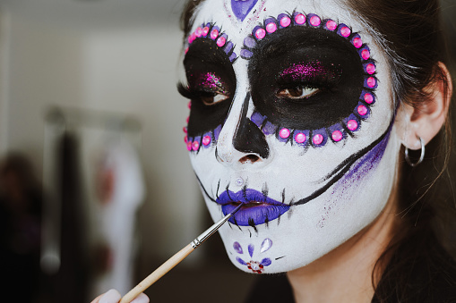 mexican Catrina, young latin woman putting on makeup her self and making a traditional skeleton for Day of the Dead or Halloween in Mexico