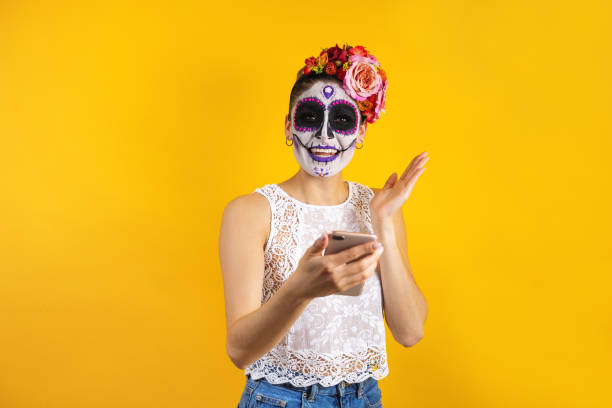 mexican catrina, portrait of young latin woman holding mobile phone for halloween party in mexico - face paint human face mask carnival imagens e fotografias de stock