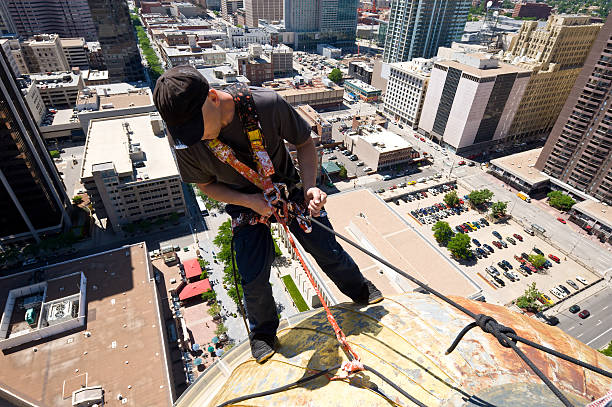 Man Rappelling Off Building Denver Colorado.  Man uses ropes, harness and other safety equipment to descend down and paint dome.  High risk worker several hundres feet up in downtown Denver with skyscrapers and office building all around.  Wide angle capture.  Converted from 14-bit Raw file.  sRGB color space.
