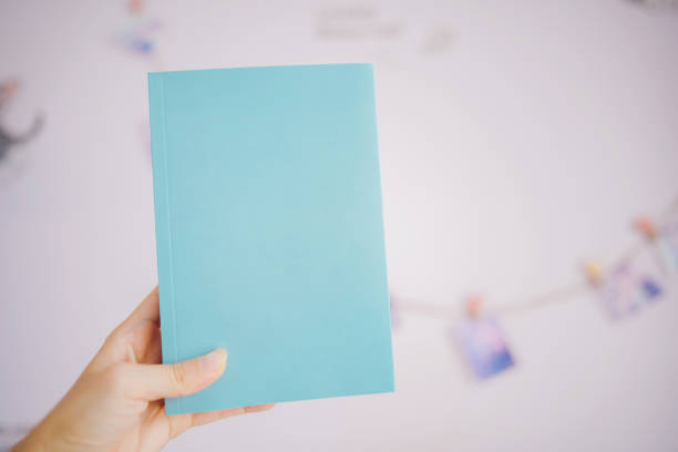 istock Hand holding a blue paperback book with blank cover with space to place text. 1344183439