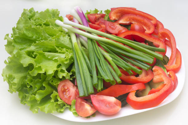 chopped green onions, tomatoes and lettuce lie on a white plate stock photo