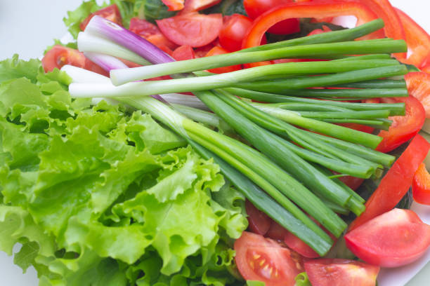 chopped green onions, tomatoes and lettuce lie on a white plate stock photo