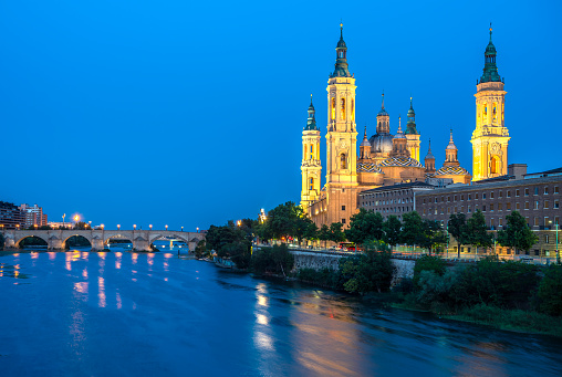 The Cathedral-Basilica of Our Lady of the Pillar along the Ebro river in Zaragoza, Spain at night.
