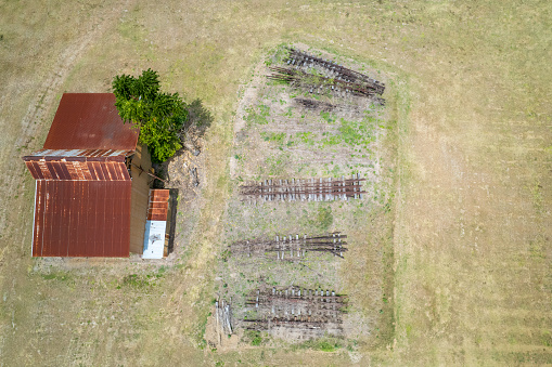 Aerial looking down onto old discarded train tracks stacked in front of a vintage rusted shed that was once part of Finch Hatton mill, Mackay, Queensland