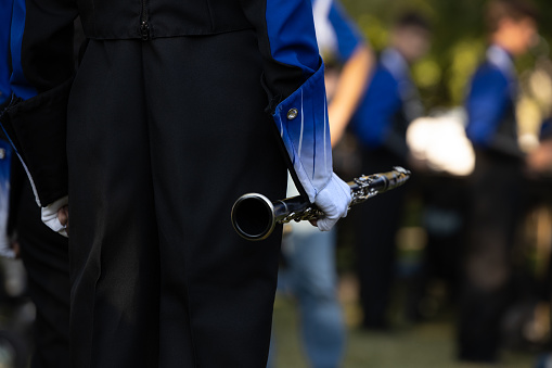 A marching band member holds a clarinet in their right hand.