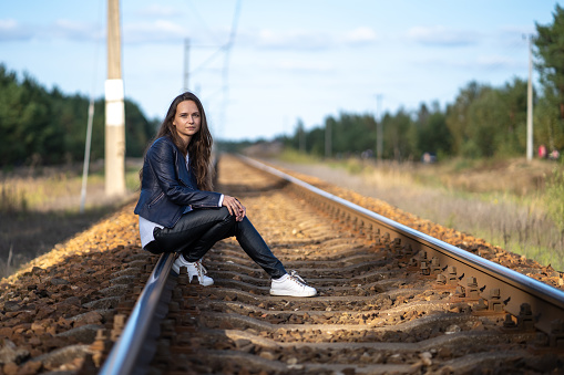 A young beautiful single woman is sitting on the railway tracks waiting for a train locomotive on a clear summer day