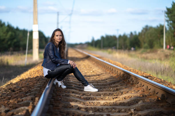 A lonely woman is sitting on the railway tracks waiting for a train locomotive A young beautiful single woman is sitting on the railway tracks waiting for a train locomotive on a clear summer day buggy eyes stock pictures, royalty-free photos & images