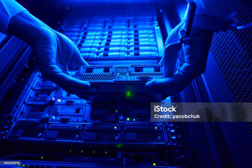 Unrecognized it engineer find and troubleshooting server computer in data center Close up low angle portrait of man hands holding HDD disk while connected it to optic port Spatholobus Suberectus Dunn Stock Photo