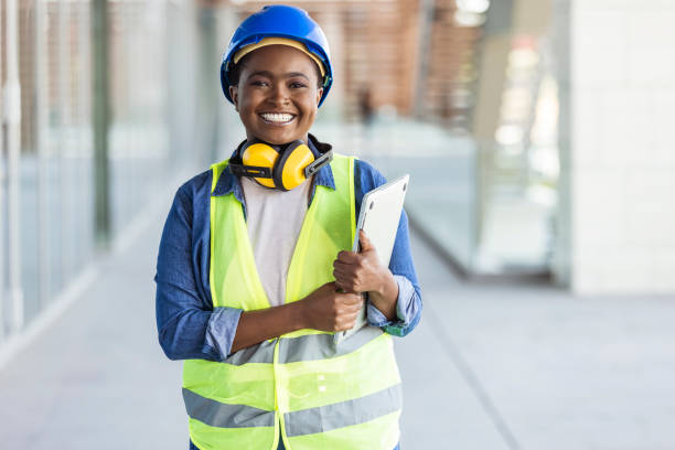 Successful confident architect at construction site Portrait of woman engineer at building site looking at camera with copy space. Mature construction manager standing in yellow safety vest and blue hardhat with crossed arms. Successful confident architect at construction site african american architecture stock pictures, royalty-free photos & images