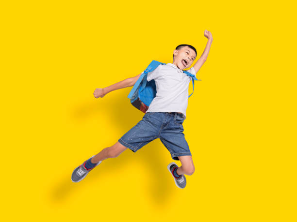 Happy student boy jumping.Isolated on yellow background. stock photo