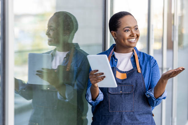 portrait d’une serveuse heureuse debout à l’entrée du restaurant tenant une tablette numérique. - présentateur de programmes télé photos et images de collection