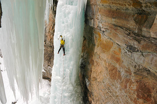 Ice Climber Extreme Adventurer on Steep Frozen Waterfall. Tecnical climbing on the Rigid Designator, Vail, Colorado.  Steep waterfal frozen ice with single athletic male person on it leading.  Wearing yellow technical jacket swinging ice axe.