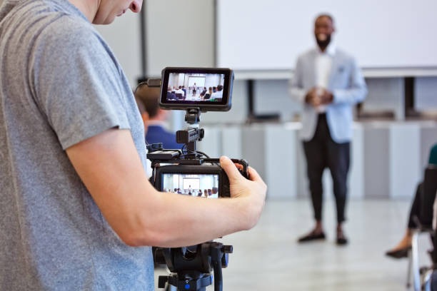 Business semiar in the convention center Group of business people during conference sitting on chairs in the convention center and listening to businessman. Focus on video camera. filming stock pictures, royalty-free photos & images