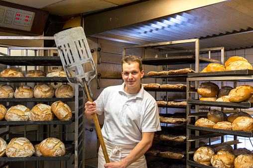 One baker posing in his bakery bakehouse in the early morning between fresh baked artisan bread