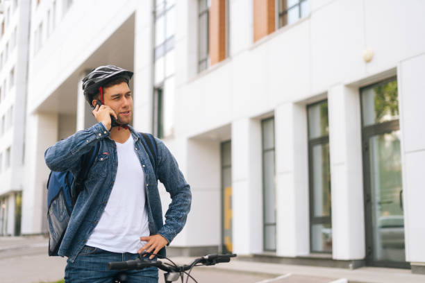 istock Medium shot of handsome courier male with thermal backpack talking on mobile phone to customer, looking for address to deliver online order. 1344219476