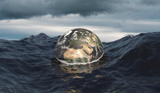 The globe sinks into the ocean as symbol for rising sea level because of global warming and pollution. Stormy ocean and dramatic sky.
