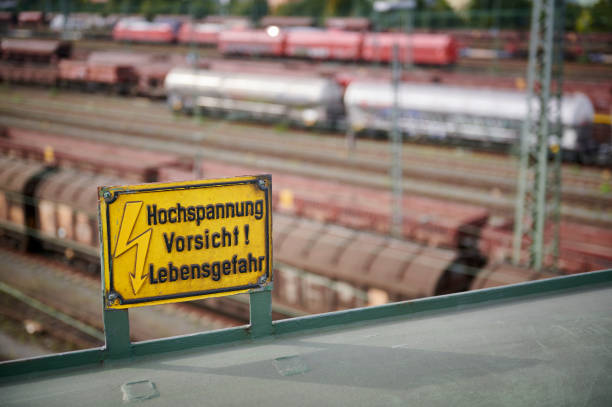 High voltage warning sign, a freight train station in the background, Germany.