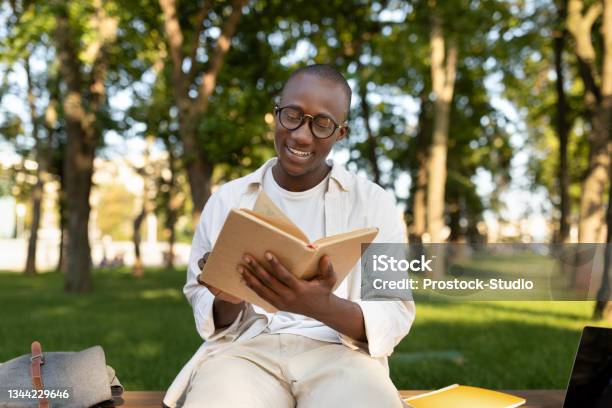 Happy African American Student Guy Reading Book Outdoors Preparing For Lectures While Sitting In University Campus Stock Photo - Download Image Now