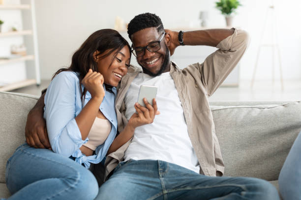 istock African american couple sitting on couch, using cellphone 1344229863