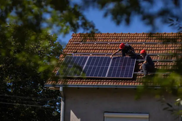 Blue collar workers installing solar panels on roof of house