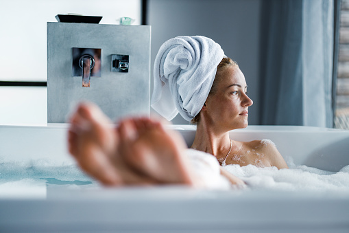 Young woman with hair wrapped in a towel enjoying while having a bubble bath.