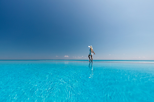 Carefree woman having fun while walking on the edge of an infinity pool in summer day. Copy space.