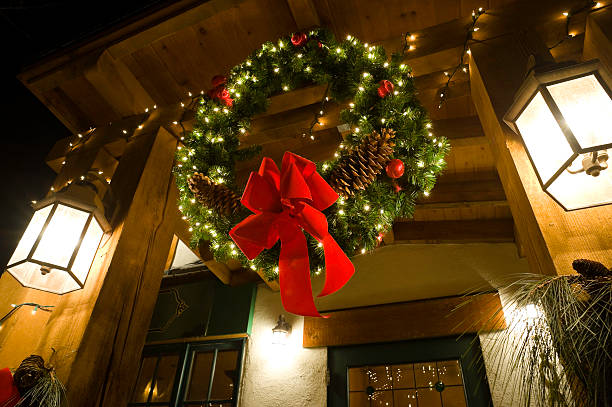 A decorative Christmas wreath hangs from a red ribbon, featuring festive greenery, shiny ornaments and textured ribbon elements. The minimalist composition on a vivid red backdrop creates a calm, inviting and joyful holiday mood, suitable for Christmas decoration themes and winter celebration imagery.