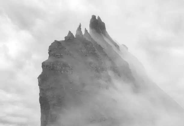 Photo of Mystical foggy lansdcapes along the coast of Vagar Island, Faroe Islands. The rocky peaks of Tindholmur (near Mykines) island enveloped by thick fog