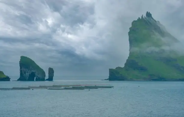 Photo of Mystical foggy lansdcapes along the coast of Vagar Island, Faroe Islands. The rocky peaks of Tindholmur (near Mykines) island enveloped by thick fog