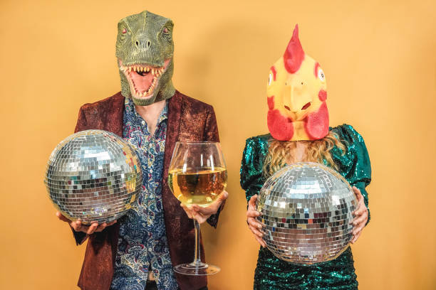 crazy couple having fun celebrating new year eve party holding disco balls and glass of wine - focus on t-rex and chicken mask - tavuk kostümü stok fotoğraflar ve resimler