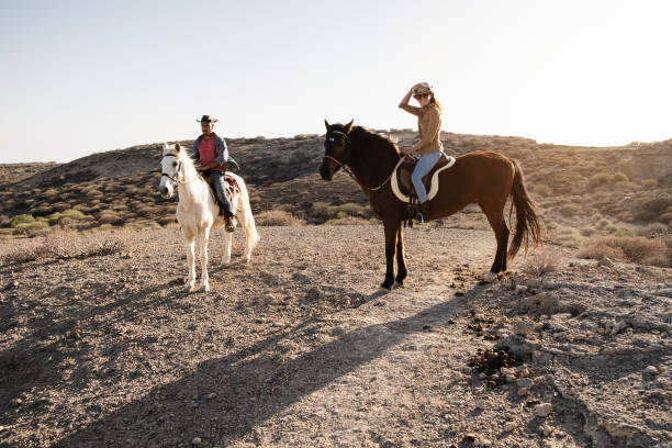 istock Young couple riding horses doing excursion at countryside during sunset time - Main focus on woman face 1344236837