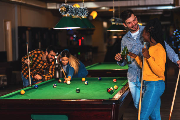 quattro amici sorridenti nel bar che giocano a biliardo insieme. - pool game pool table aiming men foto e immagini stock