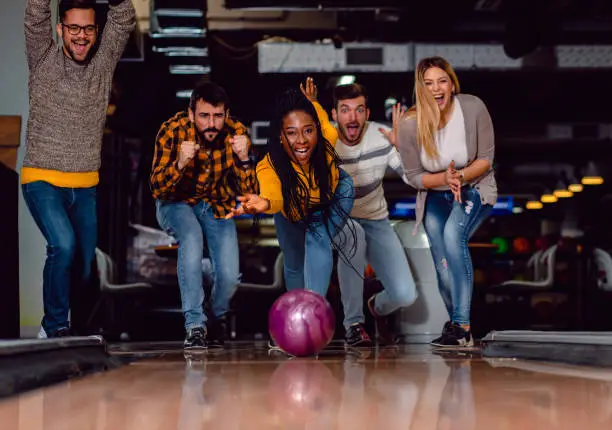 Photo of Group of friends enjoying time together laughing and cheering while bowling at club.