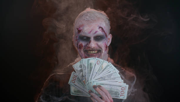 Scary sinister Halloween zombie wounded undead man with money dollar cash banknotes smiles terribly Creepy man with bloody scars face, Halloween stylish zombie make-up. Scary wounded undead guy with money dollar cash banknotes smiles terribly. Voodoo rituals. Thematic party. Sinister beast, monster devil costume stock pictures, royalty-free photos & images